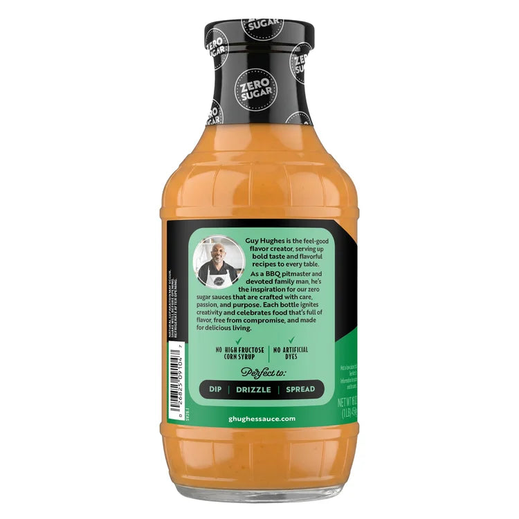 A clear bottle of Guy Hughes' zero-sugar sauce features a black cap and a green label with text highlighting its flavor, uses, and the creator's passion for cooking and family.
