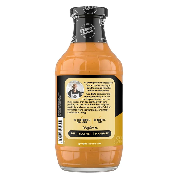 A clear bottle of Guy Hughes' zero sugar sauce features a label with his photo, a description of the product's purpose, and notes on its ingredients, emphasizing its use for dipping, slathering, and marinating.