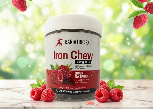 A container of Bariatric Pal Iron Chew dietary supplement, labeled "Sour Raspberry," sits on a marble surface surrounded by fresh raspberries, with a soft-focus green background.