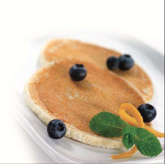 Two golden pancakes are placed on a white plate, garnished with fresh blueberries, a sprig of mint, and a twist of orange peel.