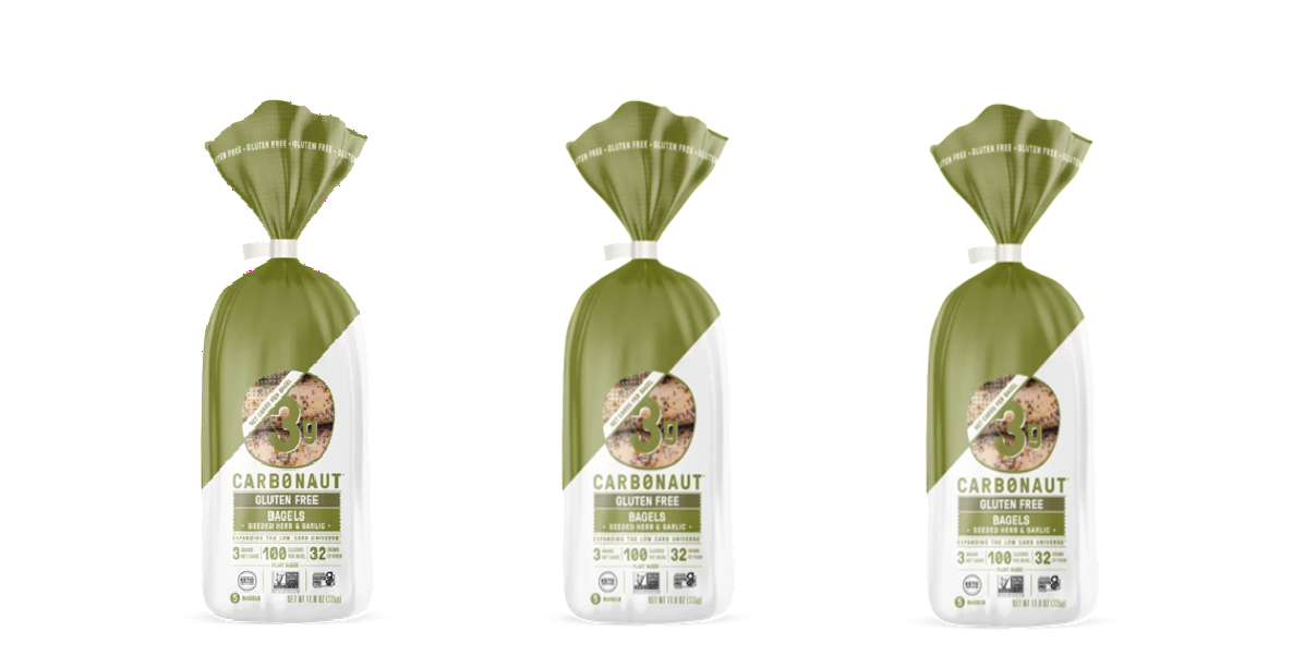 Three bags of Carbonaut gluten-free bagels are displayed, each featuring a green and white design with a label indicating they contain 3 grams of protein and are flavored with seeded herb and garlic.