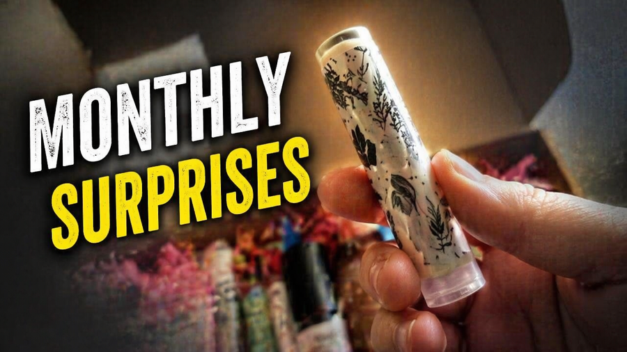 A hand holds a decorated lip balm tube in front of a colorful box filled with other beauty products, with the text "Monthly Surprises" prominently displayed in the background.